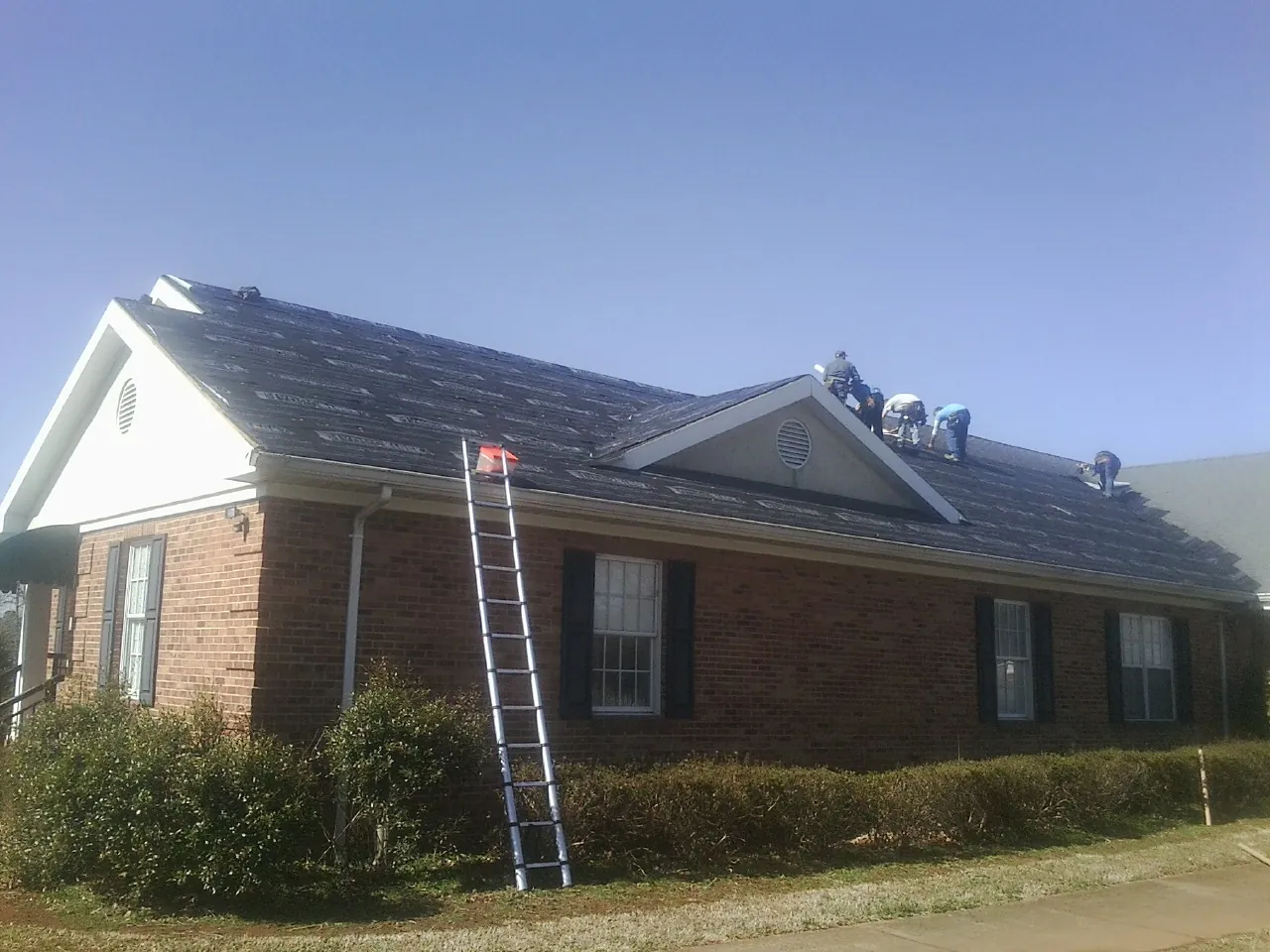 Crew tearing shingles off a brick ranch roof with a ladder set — Emergency Roof Repair work by our crew in Fortville