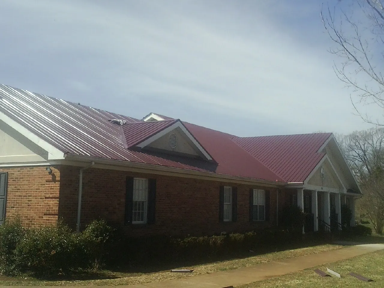 Red metal roof with gabled entries on a long brick building, from a Hail Damage Roof Repair job in Fortville