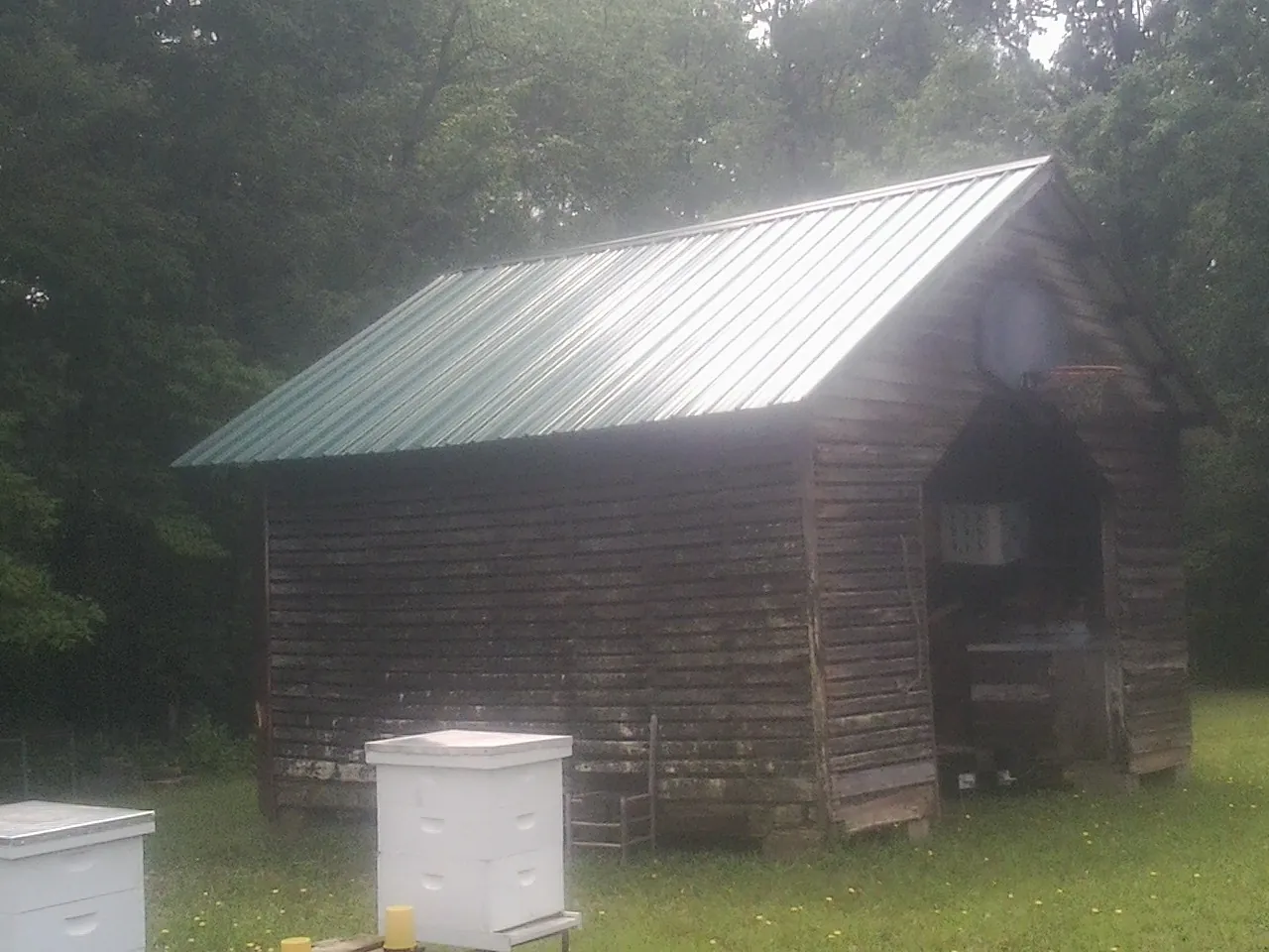 Green metal roof on a weathered barn beside stacked beehives in Fortville