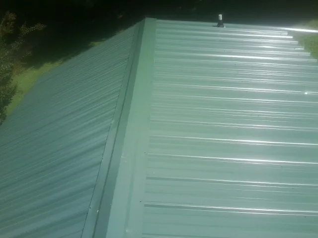 New green metal panels meeting at the ridge of a roof — Flat Roof Repair work by our crew in Fortville