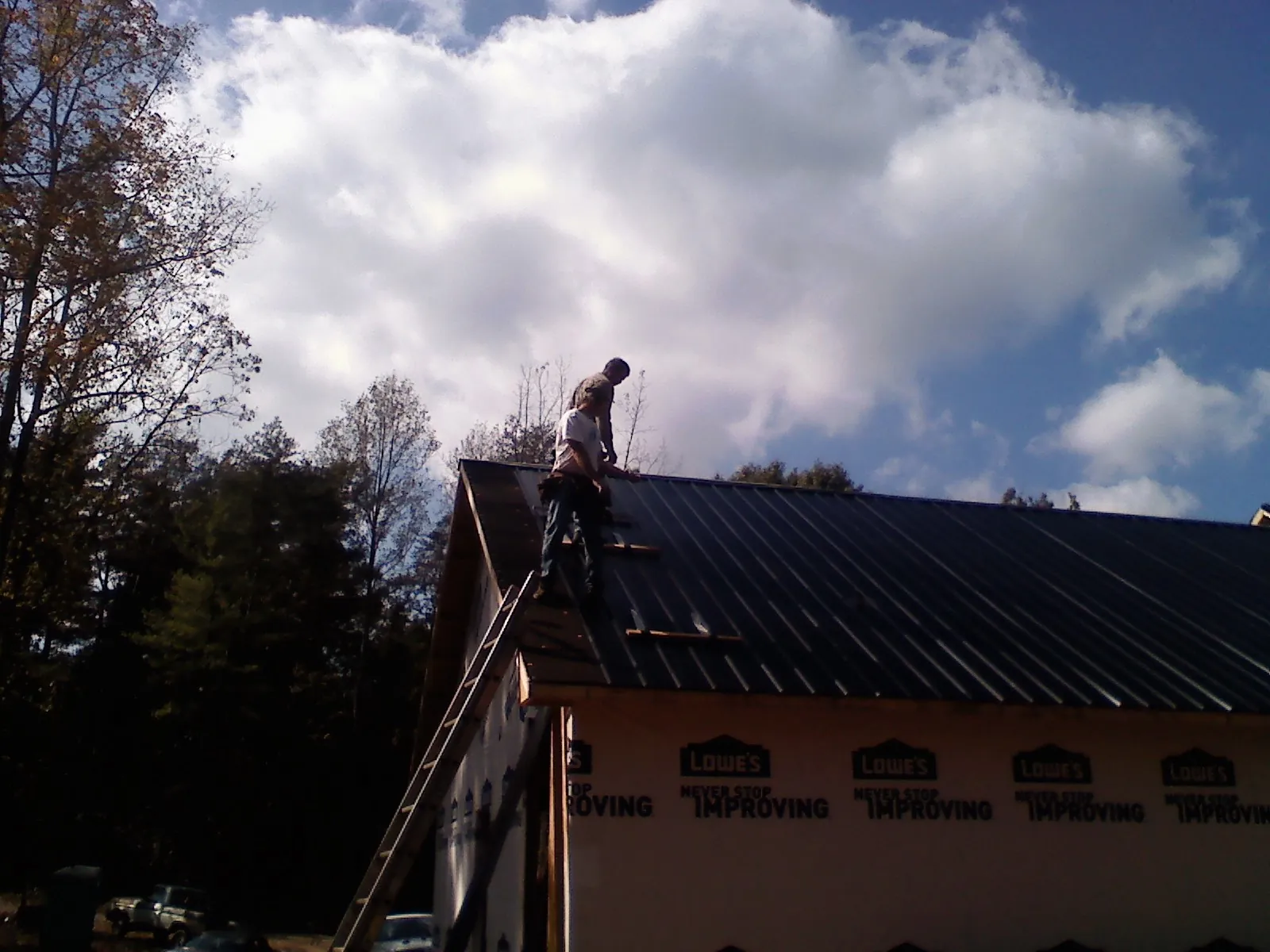 Roofer fastening dark metal panels high against a cloudy sky, from a Roof Inspection job in Fortville