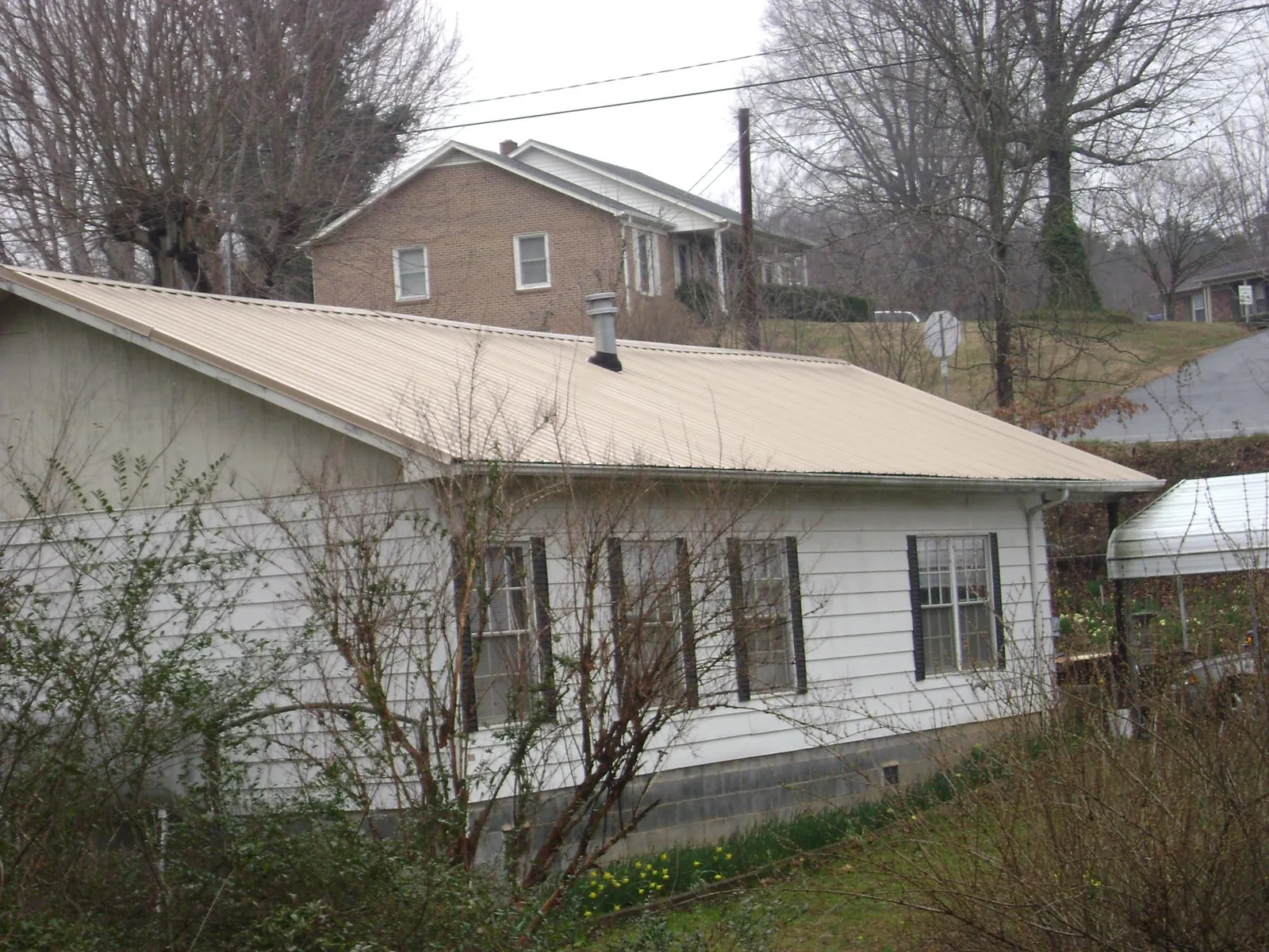 Tan metal roof on a white sided house set into a hillside — Commercial Roofing by Roofing Brothers in Fortville